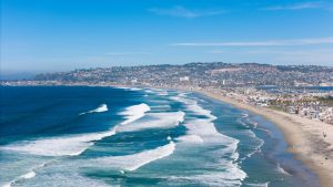 A breathtaking aerial shot of San Diego's coastline, capturing waves and cityscape under a clear sky. Blog post about taking a trip to San Diego