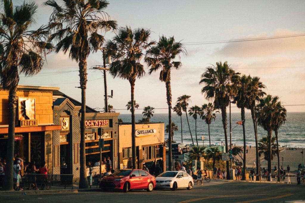 vehicles parked near tree and building near the ocean near the beach in california